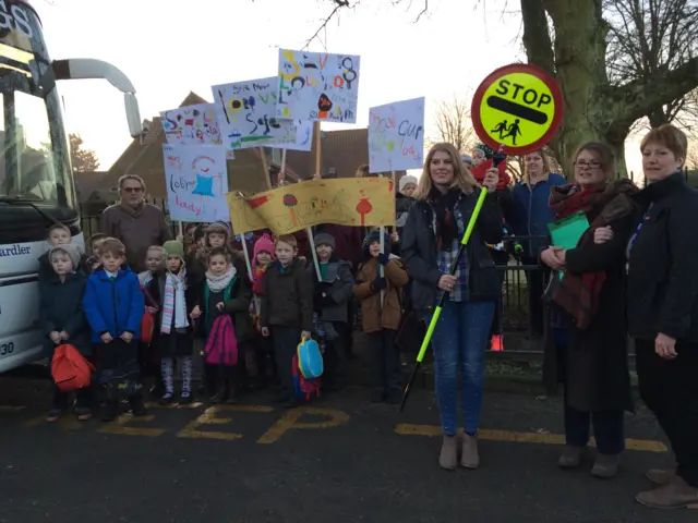 Parents and pupils stand outside the school holding banners