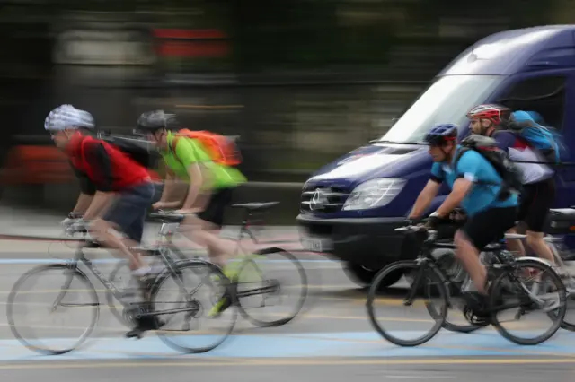 Blurred image of four cyclists and a blue van