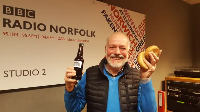 Bill Russell, in Radio Norfolk studio, holding a bottle of beer and two bread rolls