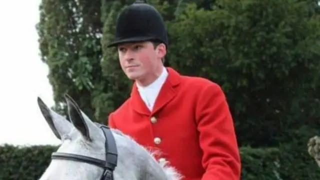 Charles Carter in red riding jacket, black riding hat, seated on grey horse