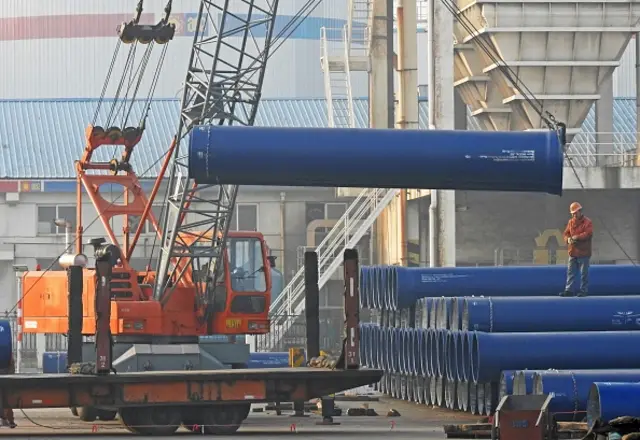 Chinese workers loading steel pipes