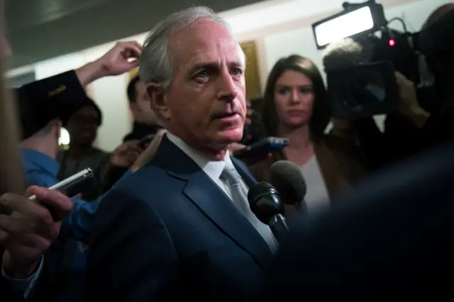 Bob Corker is pictured in a blue suit, surrounded by reporters with microphones and cameras, earlier in January.