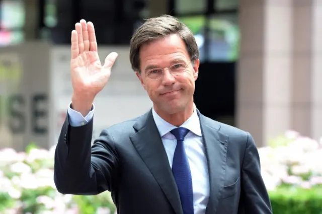 Netherlands PM Mark Rutte waves to camera in a sunny outdoor environment in front of a building