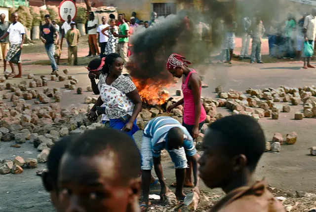 Women walk past a burning barricade set up by protestors in the Nyakabiga neighborhood of Bujumbura on July 21, 2015.