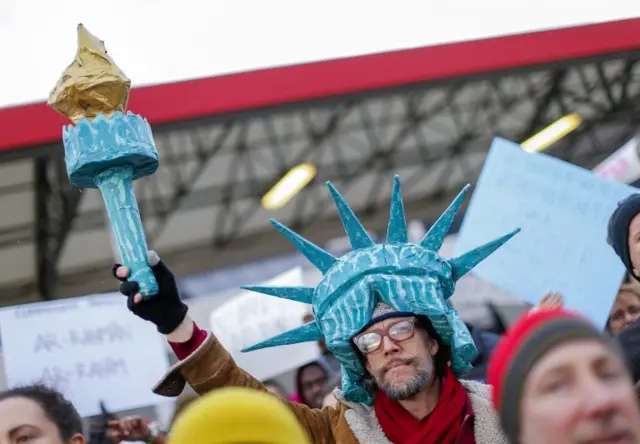 A man dressed as the statue of liberty, bearing her iconic torch aloft, takes part in one protest