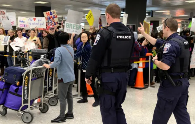 Police direct arriving passengers past dozens of pro-immigration demonstrators who cheer and hold signs