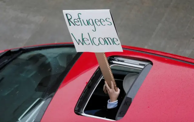 A man holds a sign reading 'refugees welcome' through a sunroof