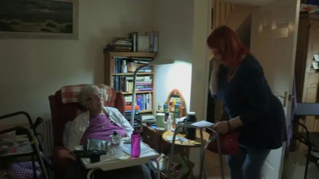 Elinor Walker, seated, with a tray on wheels over her lap - Sue standings nearby