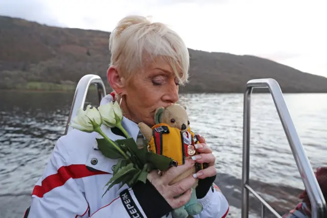 Gina Campbell on Coniston, holding a teddy bear mascot