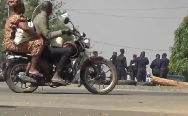 people riding past on a motorbike looking at soldiers standing at a checkpoint in Bouake