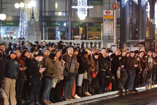 A large queue of people wait for buses at Bishopsgate in the City of London