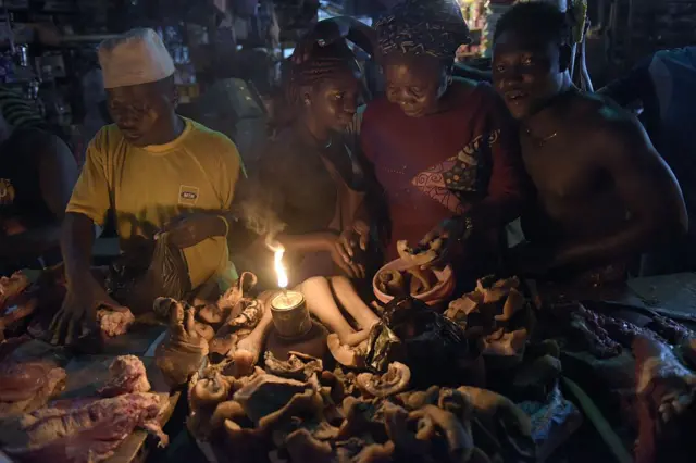 Vendors sell meat at the Oshodi night market in Lagos, late on June 6, 2015, lighting their stall with a fuel lamp in absence of electricity.