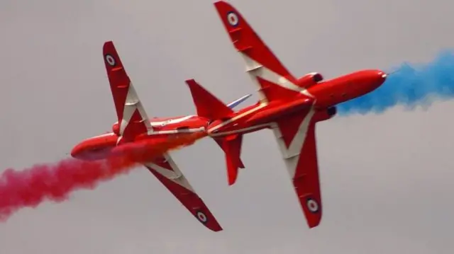 Two Red Arrows plane mid display, passing each other with red and blue smoke coming from the back of the planes.