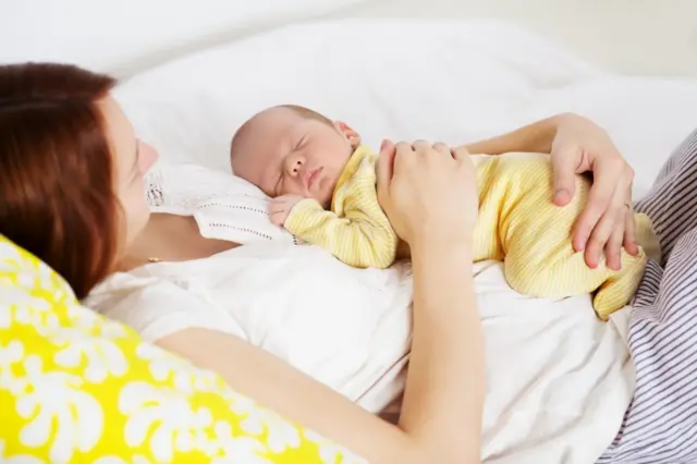 Newborn baby in yellow jumpsuit sleeps in it's mum's hands