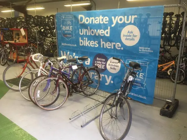 Bike racks with bikes in front of a sign asking people to donate their old bikes.