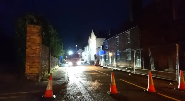 Road cones block off a street where a fire engine is parked outside a house