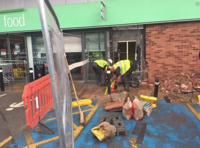 Builders clearing away rubble and rebuilding the whole in the wall.