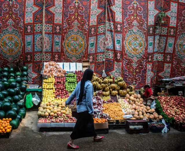 An Egyptian woman walks past a fruit stand at a market in the Egyptian capital, Cairo, on May 15, 2017.