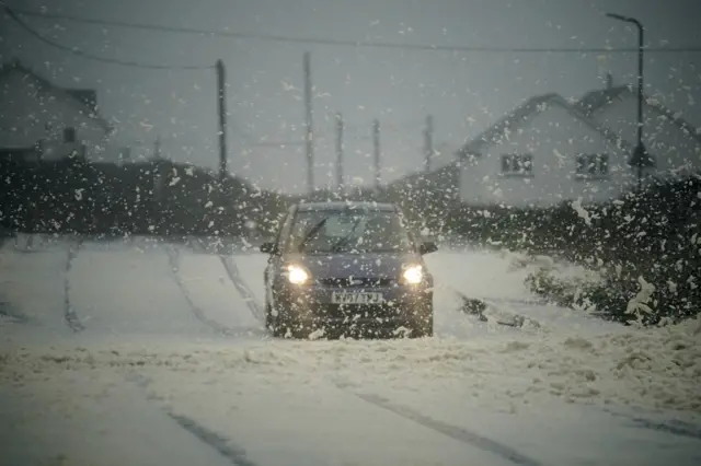 Car drives through sea foam on roads at Trearddur Bay