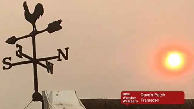 Red sun over rooftop, with weather vane