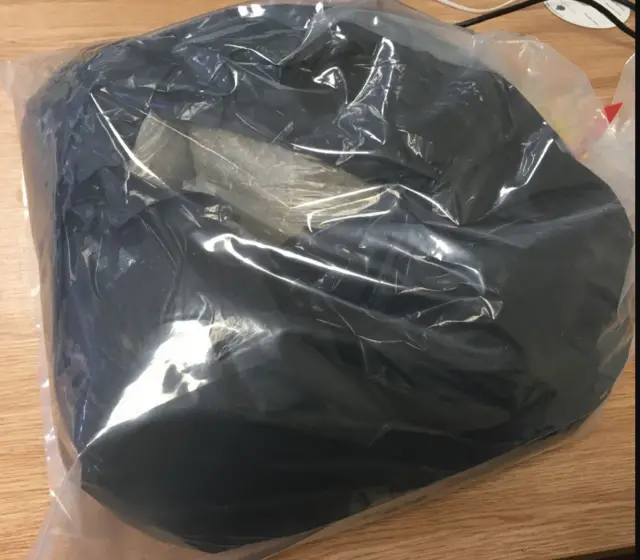 A black bag containing smaller, clear bags lies on a desk