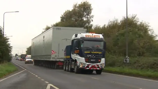 Lorry carrying large metal container.