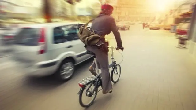 Cyclist on a bike on the road passing a car.