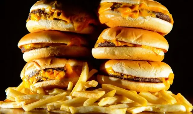 Cheese burgers piled on top of each other with chips around the side.