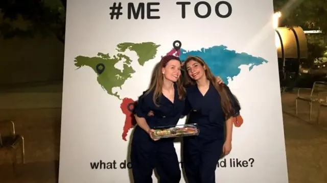 Two women infront of a map of the world with the words 'me too' above it.