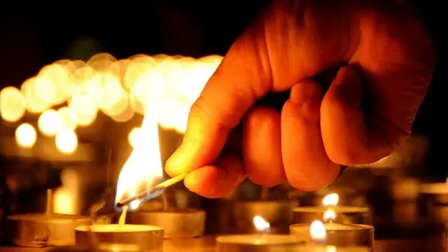 a hand holds a match which lights a candle