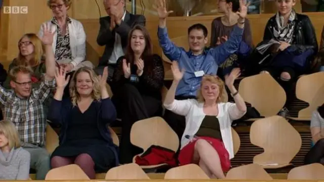 Members of the public in the gallery celebrate the passing of the British Sign Language Bill