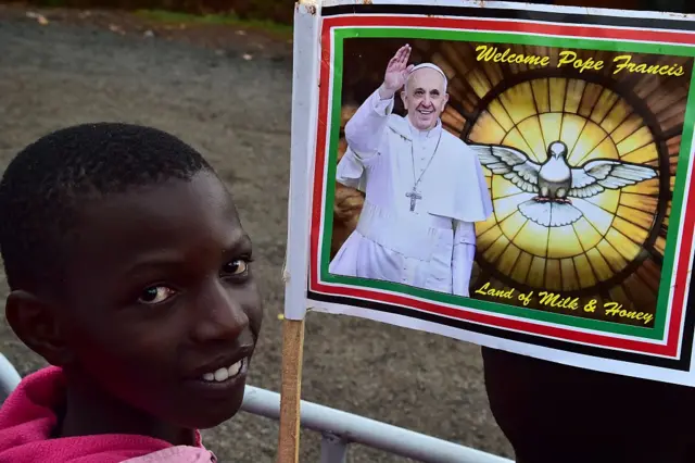 A youth holds a banner bearing an image of Pope Francis, as he waits for the arrival of the Pontiff at the Church of St Joseph the Worker at the Kangemi slum in Nairobi on November 27, 2015.