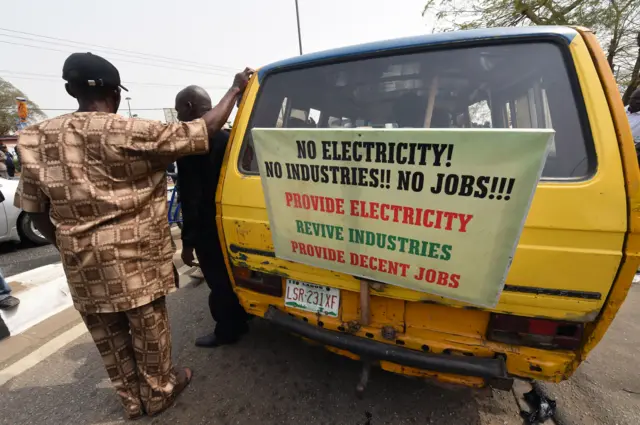 A man stands next to a placard reading 'No electricity! No industries!! No jobs!!! Provide electricity, revive industries, provide decent jobs' during a demonstration to protest against the 45 percent raise of electricity prices on February 8, 2016 in Lagos