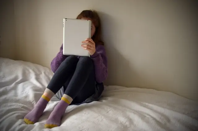 Young girl sitting on a bed, browsing the internet