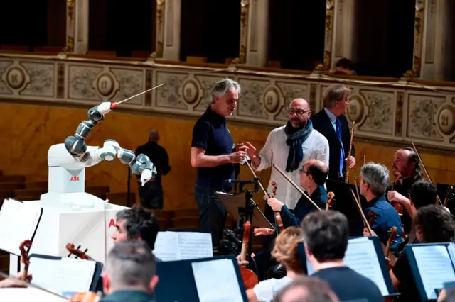 This photograph taken on September 12, 2017, shows the robot 'Yumi' conducting Italian tenor Andrea Bocelli (C) and The Lucca Philharmonic Orchestra in rehearsal for a concert for the first time at The Teatro Verdi in Pisa.