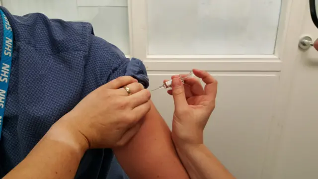 A needle hovers over a man's arm to deliver a flu vaccination.