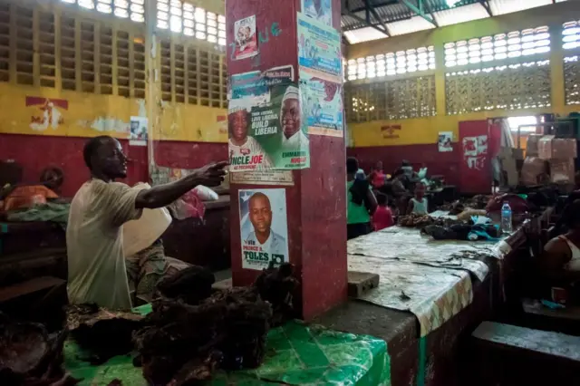 A man gestures by an electoral poster of Joseph Boakai, presidential candidate for Liberian political party Unity Party, at the Rally Time market, in Monrovia.