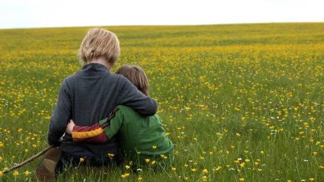 Two young boys sitting in a field hugging each other