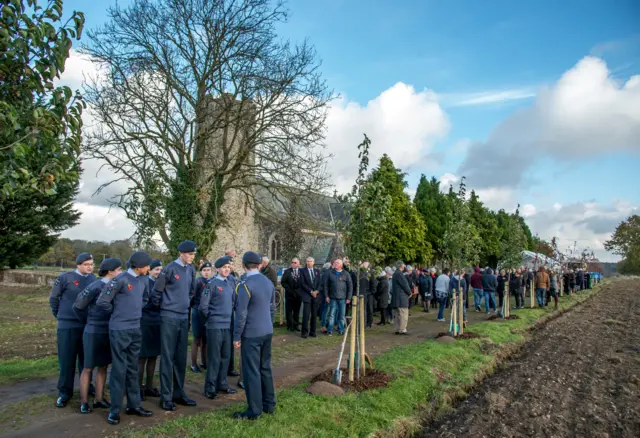 The avenue of trees by the church, with crowds of people, some youngsters in air force uniform