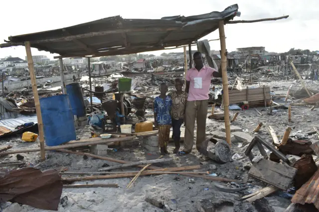 Kpose Roberts stands with his children, at his flour and pepper mill in Otodo-Gbame. They are surrounded by the rubble of what was once their community, following demolitions and forced evictions of March 2017.