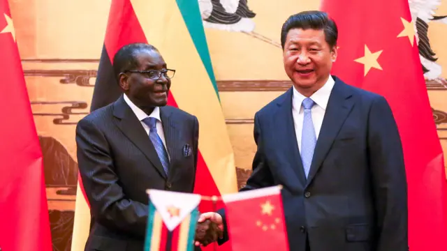 Robert Mugabe and Xi Jinping shake hands in front of a small dislay wiht both countries' flags, 2014