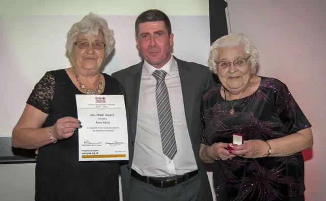 Ann Kent with her sister Edna, receives her Volunteer Award from Chris Hynes from award sponsor Brewin Dolphin.