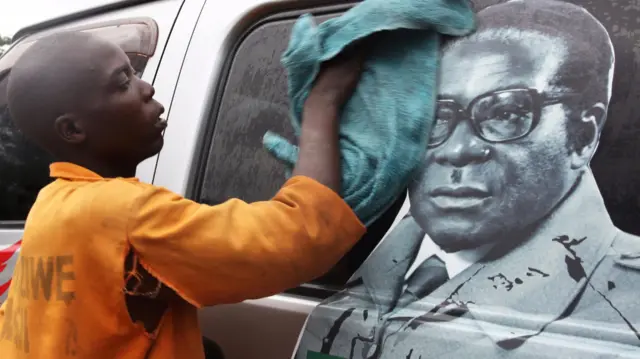 A man cleaning a vehicle with an image of Robert Mugabe on it