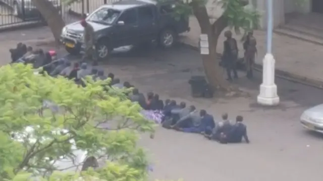 Police sitting on the ground with the army looking on