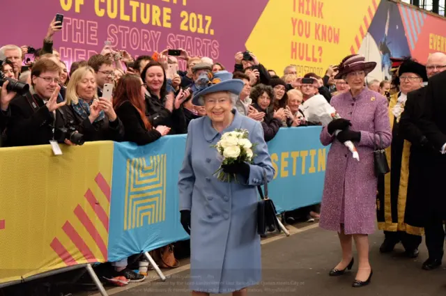 The Queen smiling with crowds of well wishers looking on.