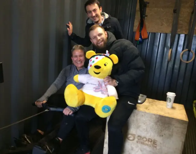 Pudsey and a woman on a rowing machine taking a selfie.