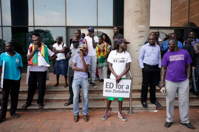 A man holds a placard reading "Ed for a new Zimbabwe" as people wait for the arrival of Zimbabwe"s former vice president and designated president Emmerson Mnangagwa in front of the Zimbabwe African National Union Patriotic Front (ZANU-PF) party headquarters in Harare on November 22, 2017