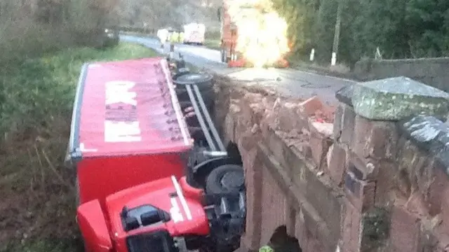 The demolished bridge and lorry lying on its side