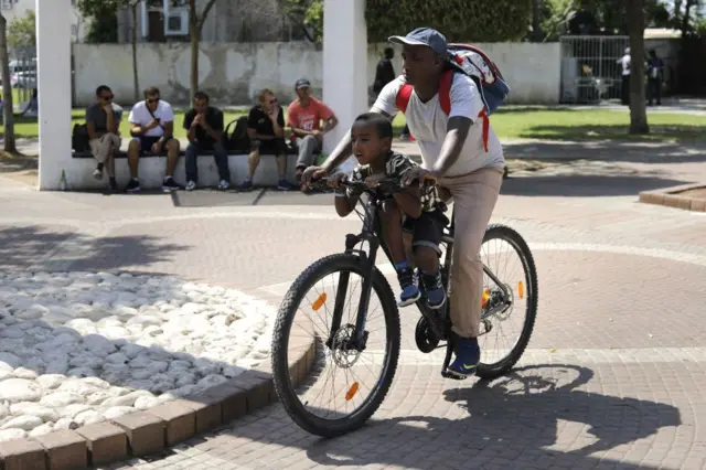 An African migrant rides a bicycle with a child near the Levinsky park street in southern Tel Aviv on September 4, 2017