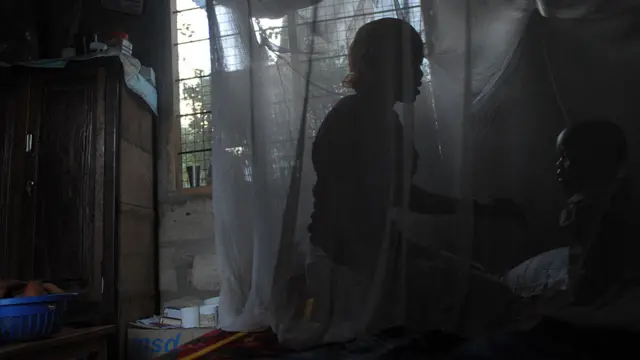 A mother and her child sit on a bed covered with a mosquito net near Bagamoyo, Tanzania - 2009